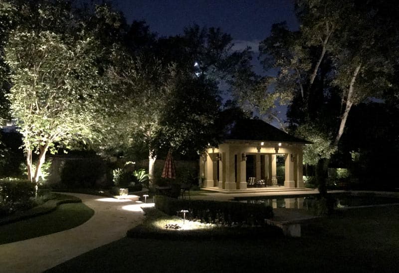 A beautiful back yard with a gazebo seen at night by outdoor lighting