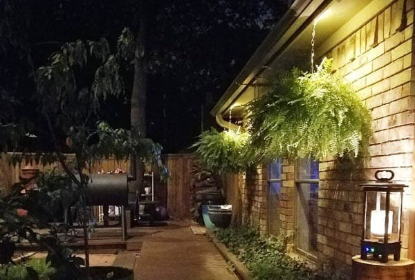 A patio with a grill and lighting for the path and to highlight hanging plants and brick of house