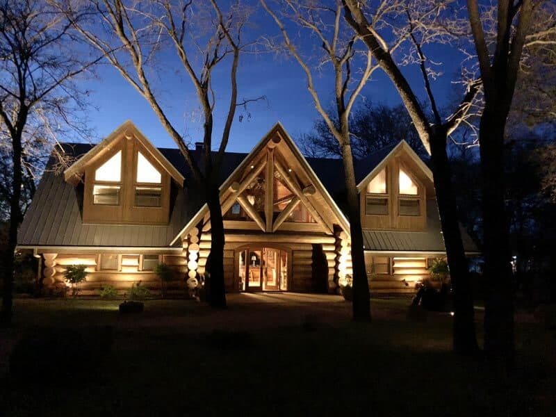a cabin in the wood lit up with exterior lighting
